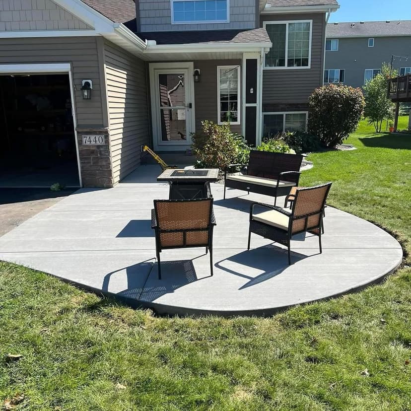 Outdoor patio featuring four wicker chairs and a fire pit, surrounded by green lawn and home.