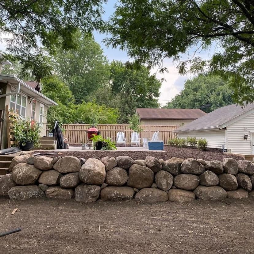 Backyard landscaping featuring a stone retaining wall, patio area, and lush greenery.